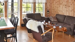 A cozy living room with a wooden floor, a sofa, a chair with a white throw, a coffee table, and a dining area with chairs and a table. - 4 Star Holiday Home in Rennebu (Rennebu)