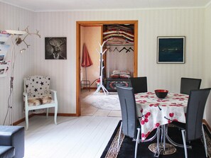 Uma área de refeições com uma mesa posta para quatro pessoas, uma cadeira branca com desenhos de estrelas, um sofá preto e um tapete estampado.