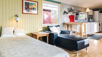 Una habitación con una cama, un sofá de cuero negro, una pequeña mesa de madera, un ventanal con vistas y una kitchenette al fondo.