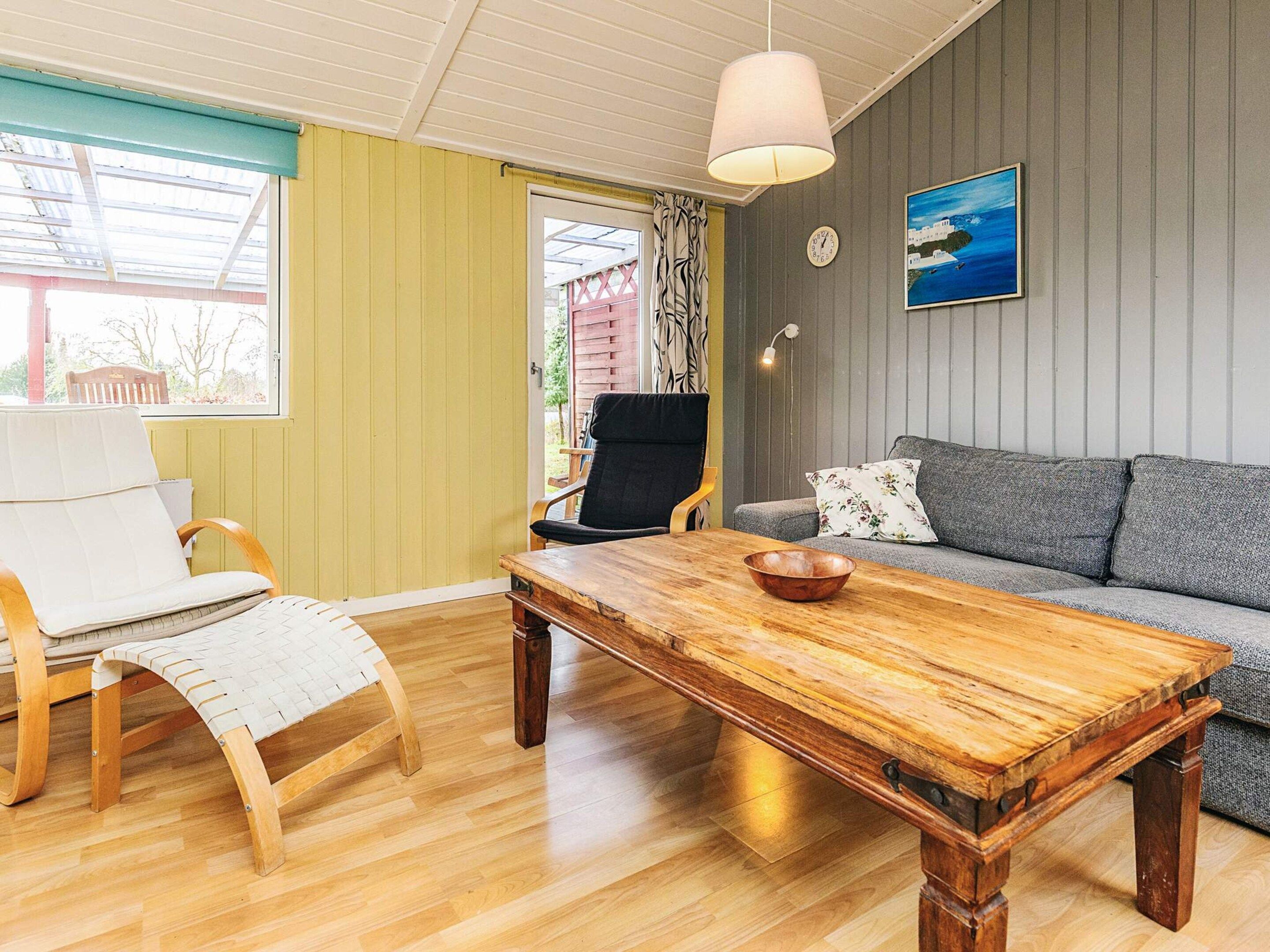 A cozy living room with a wooden coffee table, a grey sofa, a white armchair, and a wooden chair.