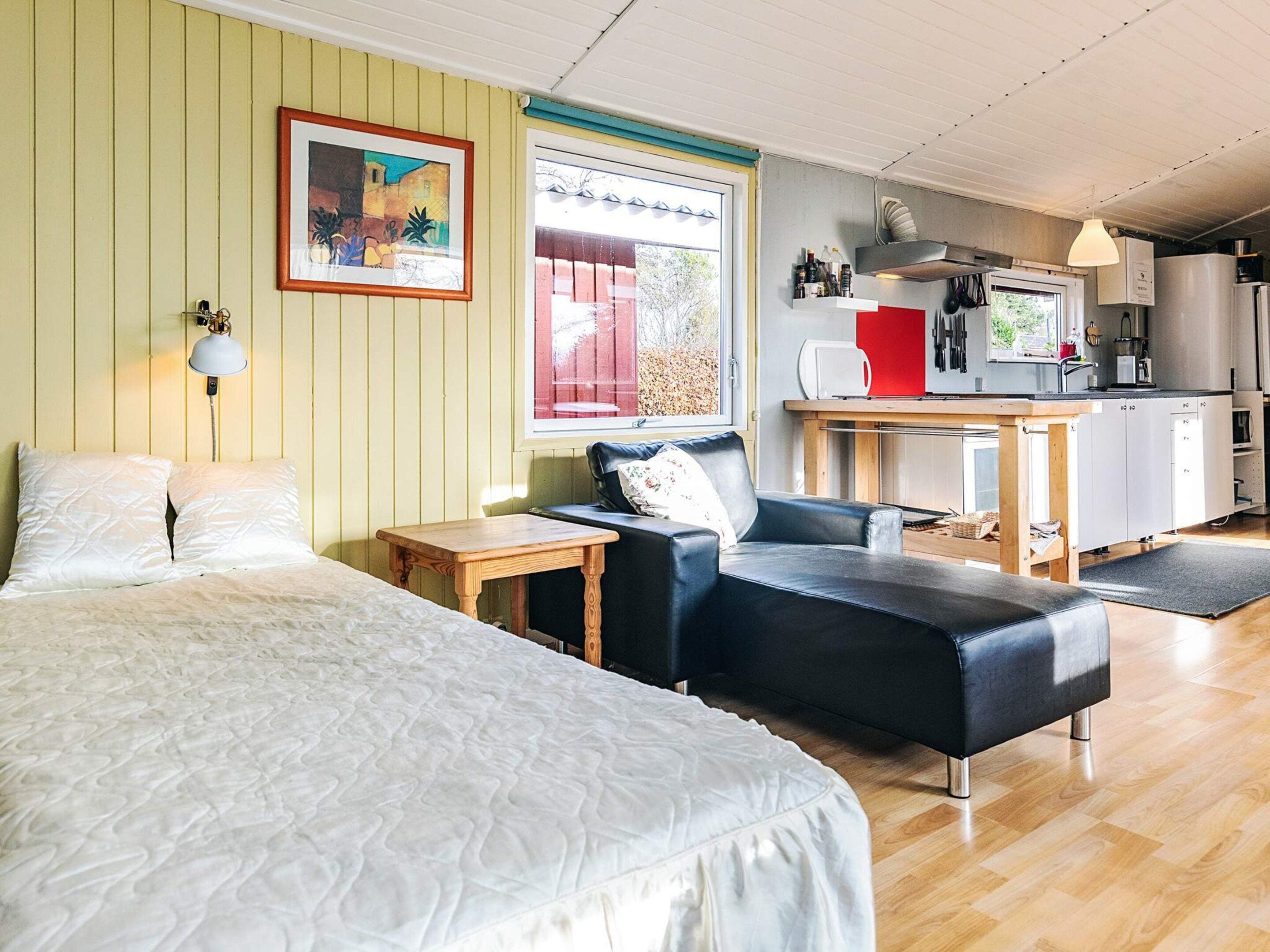 Une pièce confortable avec un lit, un canapé en cuir noir, une petite table en bois et, au fond, un coin cuisine.