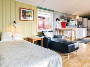 Une pièce confortable avec un lit, un canapé en cuir noir, une petite table en bois et, au fond, un coin cuisine.
