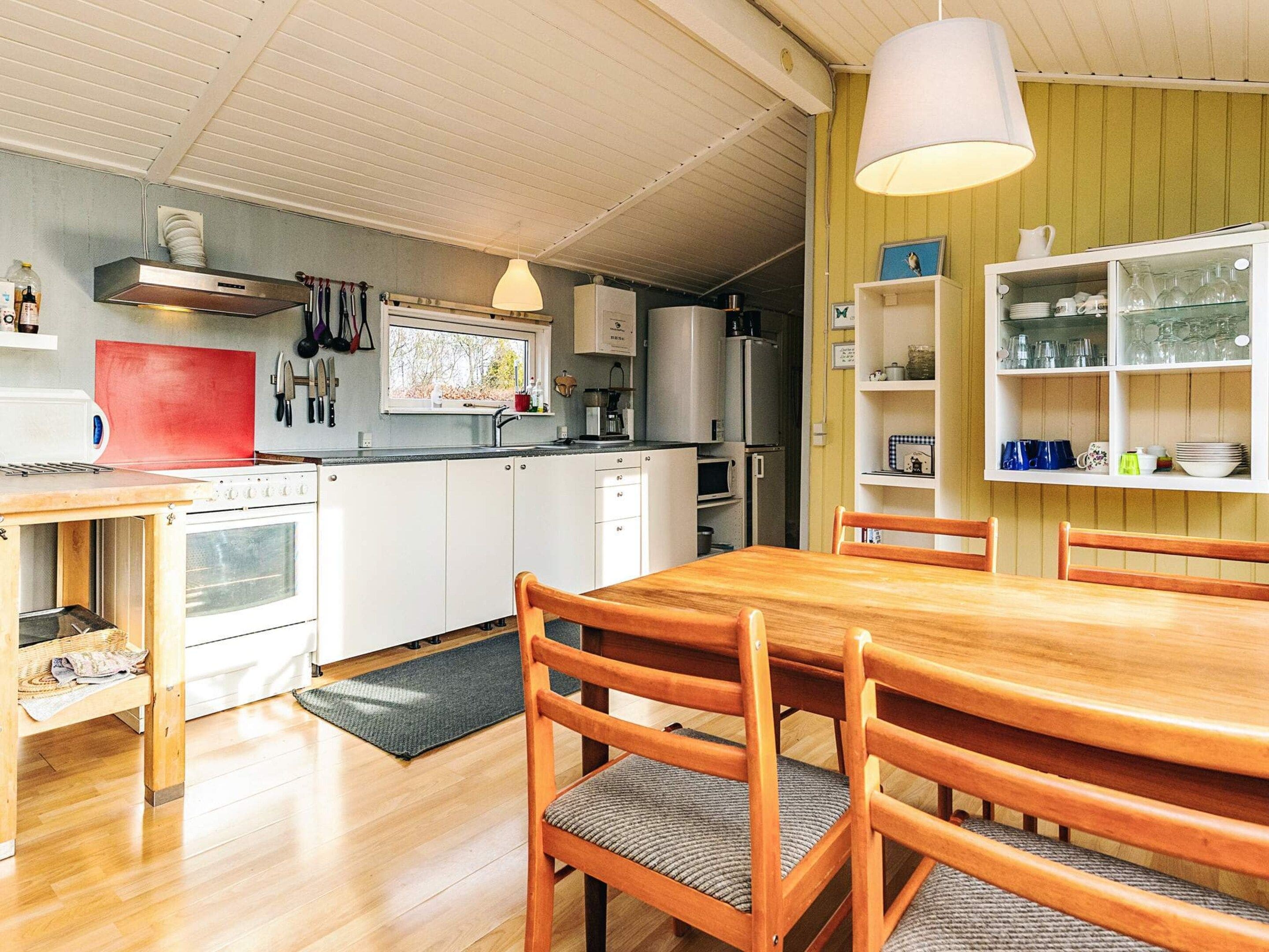 Une cuisine de taille réduite avec des meubles blancs, une table à manger en bois et un luminaire suspendu.