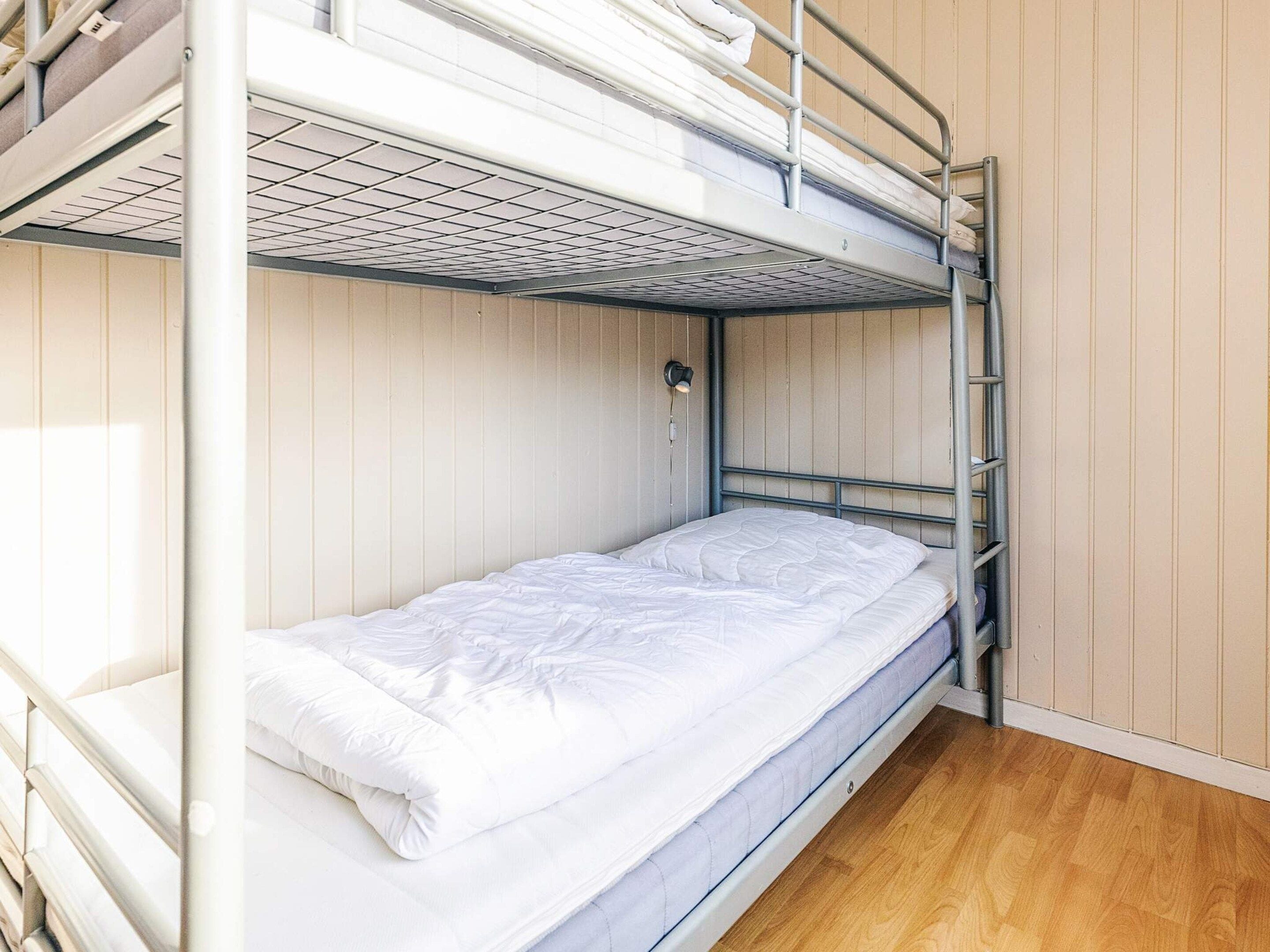 Una cama litera con colchón y almohadas, una lámpara fijada a la pared y suelo de madera.