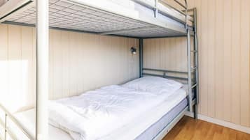 Una cama litera con colchón y almohadas, una lámpara fijada a la pared y suelo de madera.