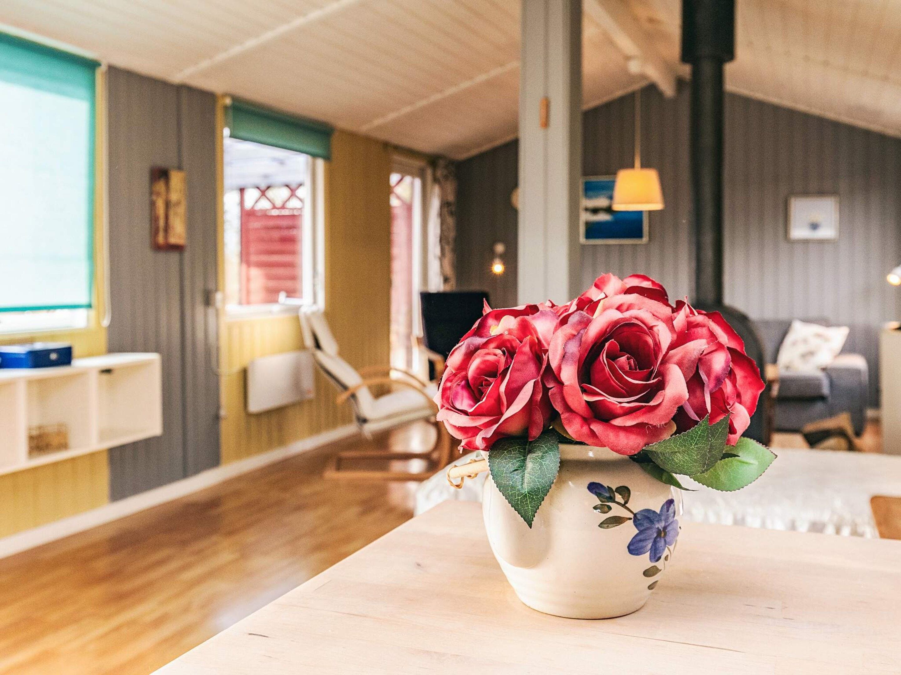 Une pièce avec un plancher en bois, une table blanche ornée d’un vase de roses rouges, une chaise et un canapé.