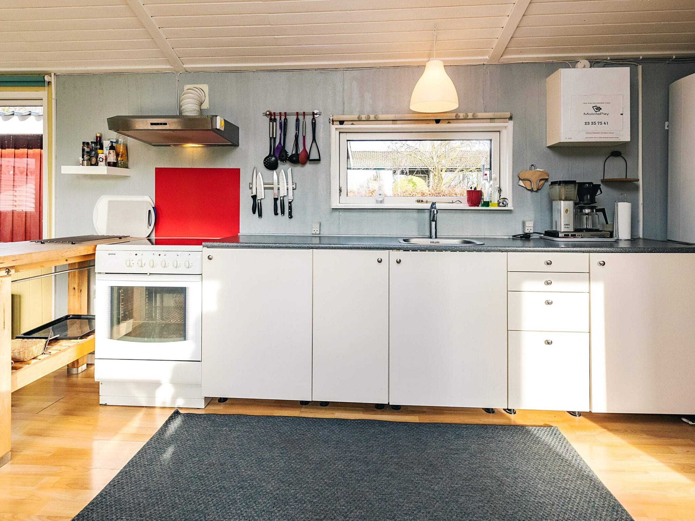 Una cocina moderna con armarios blancos, horno integrado, ventana con vistas y una lámpara colgante.