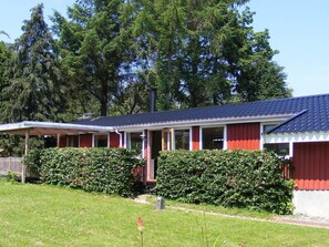 A row of red and white cabins with a covered porch area, surrounded by dense green shrubbery. - 4 Person Holiday Home in Vordingborg (Vordingborg)