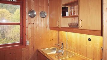 A wooden cabin kitchen with a sink, two metal bowls on the wall, and a shelf with a jar and a bowl.