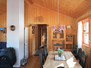 A wooden cabin interior with a dining table, chairs, a refrigerator, and a ski rack.
