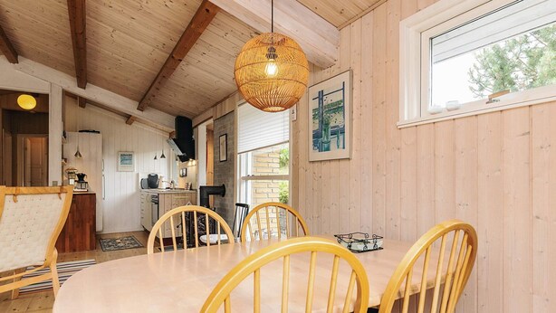 A wooden interior with a dining table and chairs, a hanging light fixture, and a window with a view of trees. - Serene Holiday Home in Zealand near Sea (Stege)