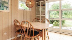 Une pièce aux murs lambrissés, avec une table ronde et des chaises, un luminaire suspendu et une vue sur la verdure grâce à de grandes fenêtres.