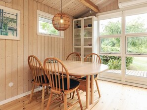 Una habitación con paneles de madera, una mesa redonda y sillas, una lámpara colgante y vistas a follaje a través de amplios ventanales.