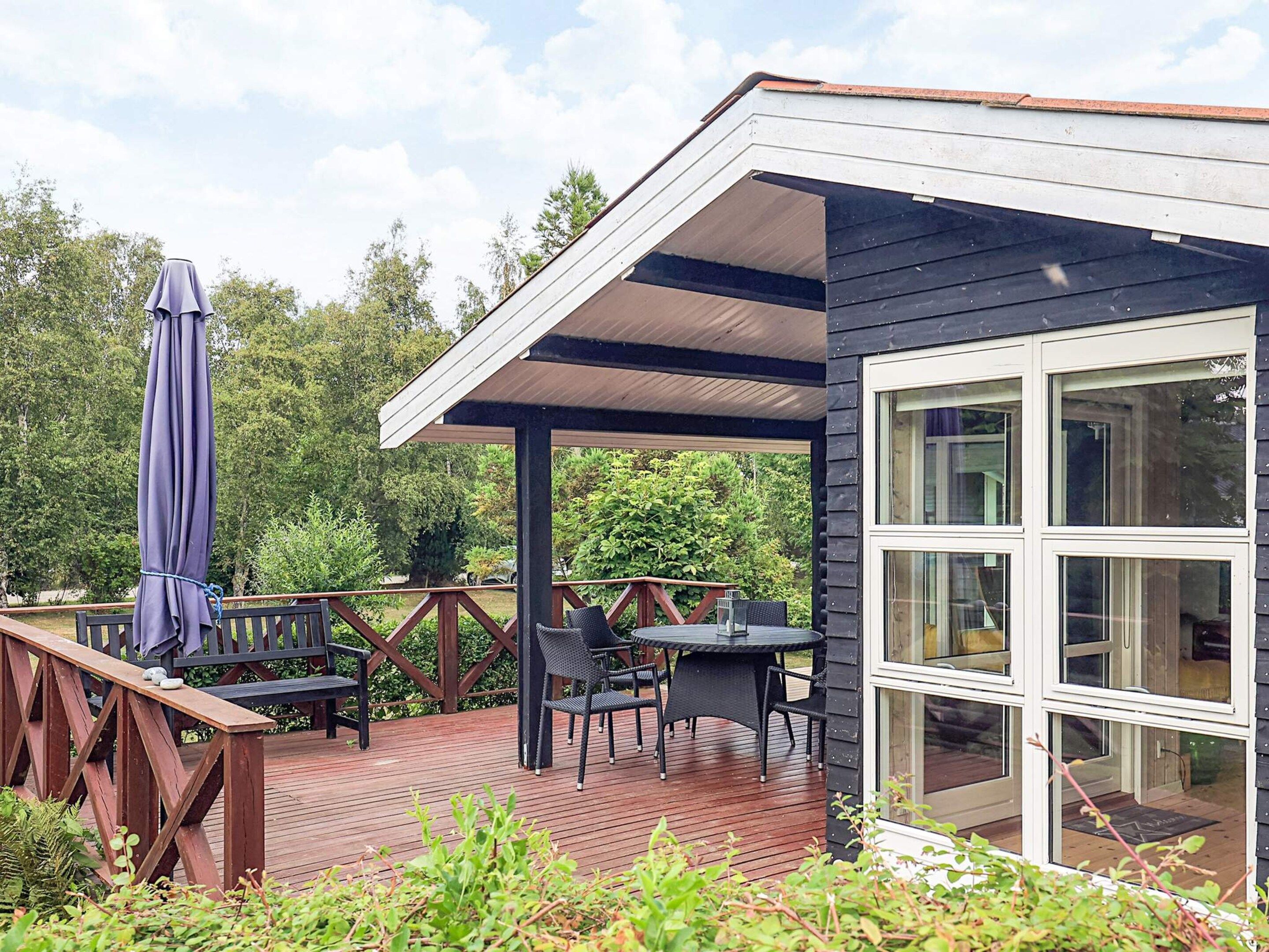A covered outdoor deck with a table and chairs, a wooden bench, and a patio umbrella.