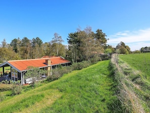 Una casa moderna con techo rojo, rodeada de un campo cubierto de hierba y árboles.