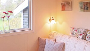 A room with a window, a wall-mounted lamp, a sofa with patterned cushions, and a framed picture on the wall. - Serene Holiday Home in Zealand near Sea (Stege)