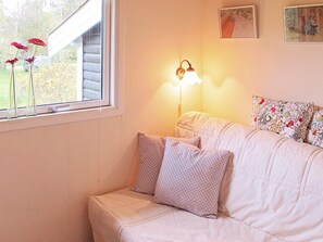 A room with a window, a wall-mounted lamp, a sofa with patterned cushions, and a framed picture on the wall. - Serene Holiday Home in Zealand near Sea (Stege)