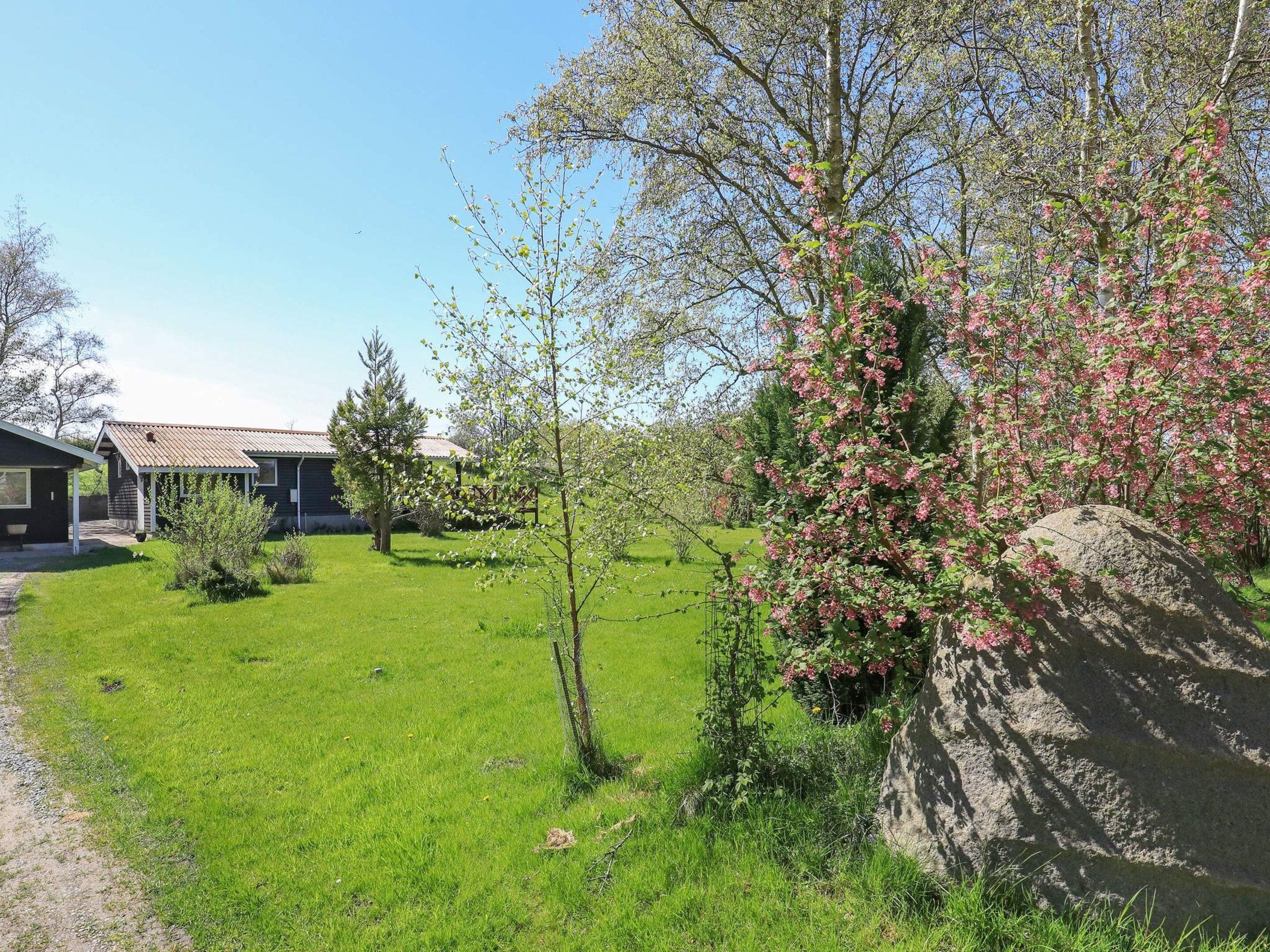 A residential property with a well-maintained lawn, a house with a tiled roof, and a large tree with pink blossoms.