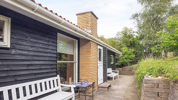 Une terrasse avec un banc blanc et une table, une petite construction en briques et un espace jardin.