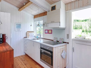 A kitchen with wooden cabinets, a stainless steel sink, a built-in oven, and a window with a view of greenery. - Serene Holiday Home in Zealand near Sea (Stege)