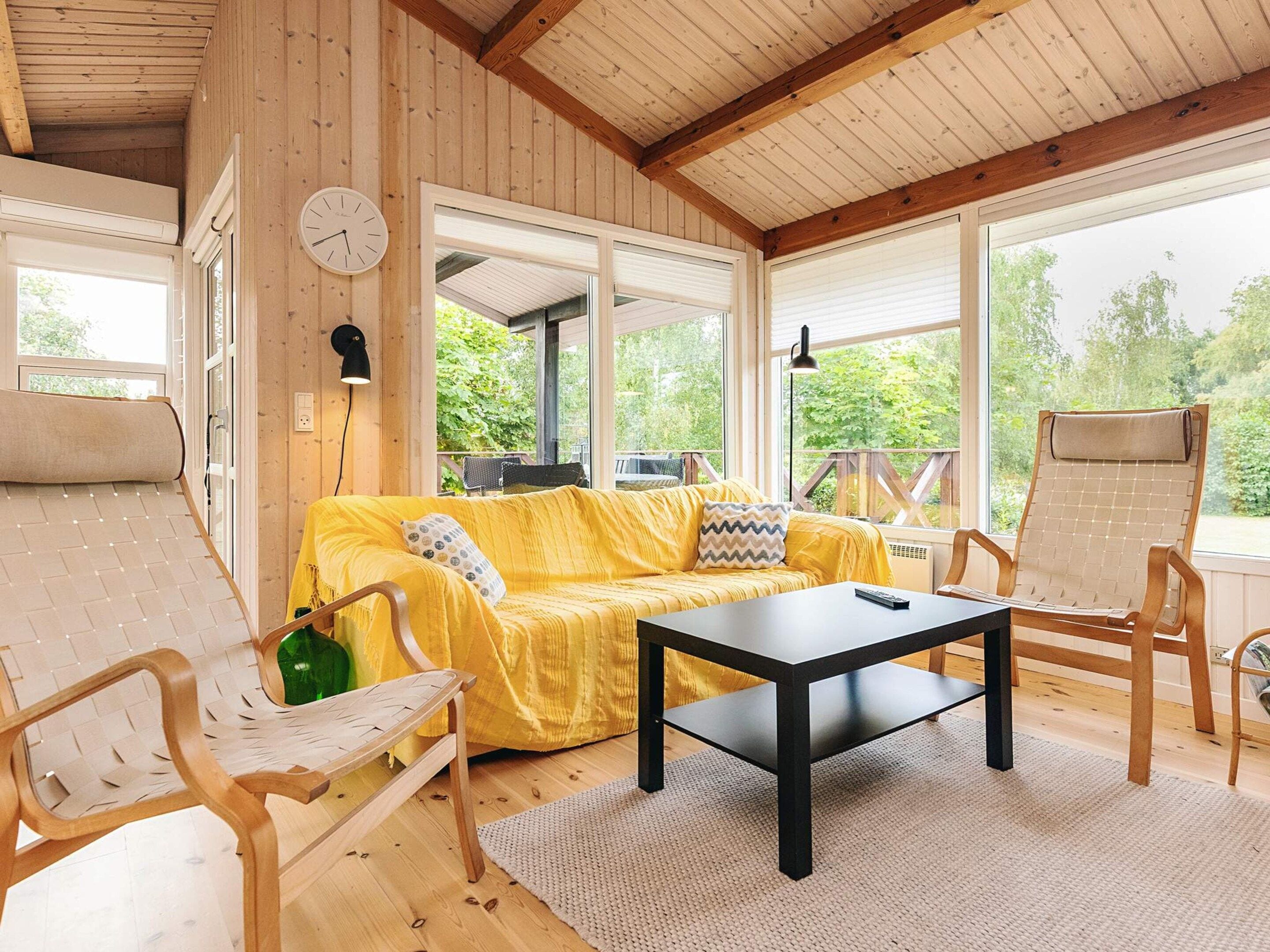 A wooden interior with a sofa, chairs, a table, and large windows.