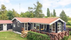 A cabin with a deck, a covered porch, and a small garden area. - Serene Holiday Home in Zealand near Sea (Stege)