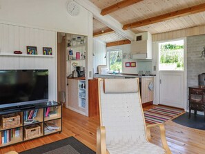 A cozy living room with a TV, bookshelf, and a woven chair. - Serene Holiday Home in Zealand near Sea (Stege)