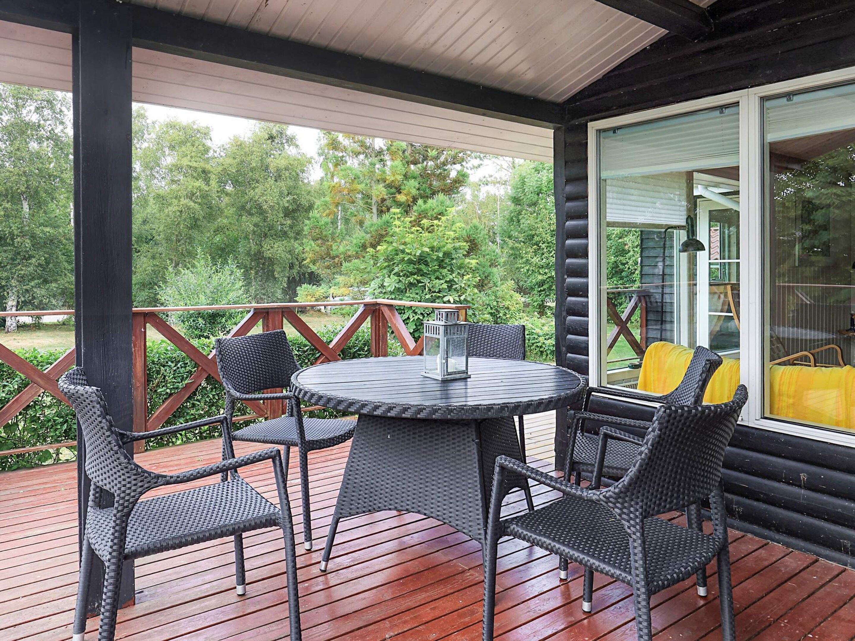 En overdækket terrasse med et rundt bord og fire stole, omgivet af en træterrasse og gelænder af glas.