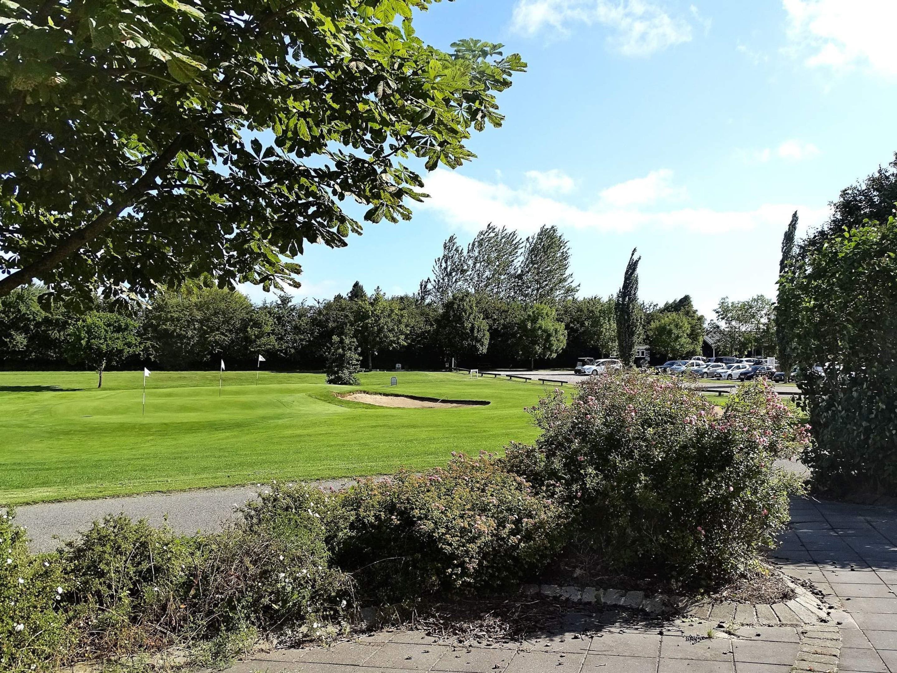 A golf course with a clear sky, trees, and a parking area.