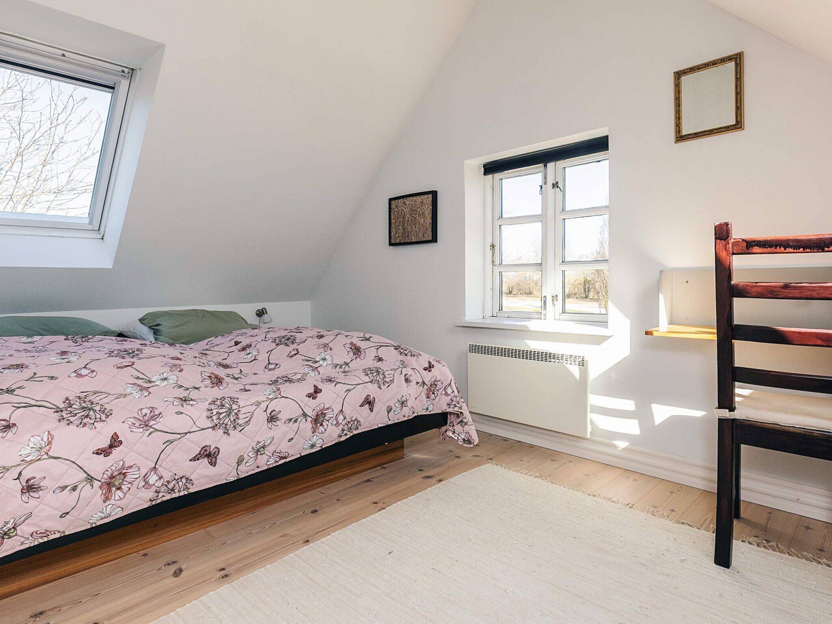 A bedroom with a bed, a window, a radiator, and a wooden chair.