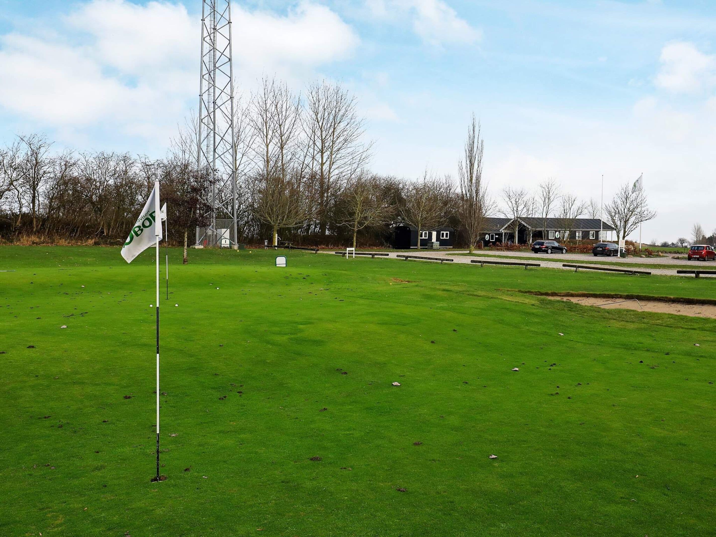 A golf course with a flag, a tall metal structure, and a building in the background.