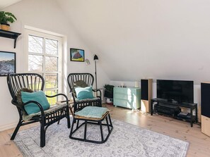 A living room with two black wicker chairs, a teal cushion, a small wooden stool, a television, and a cabinet. - 4 Star Holiday Home in Humble (Sydlangeland)