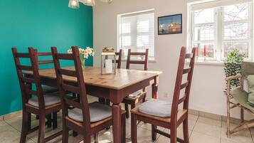 A dining area with a wooden table and chairs, a teal accent wall, and a window with blinds.