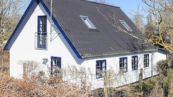 A white house with a dark roof, multiple windows, and a visible chimney.