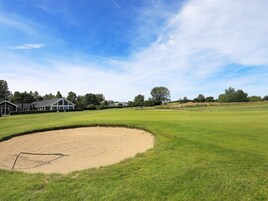 A golf course with a sand bunker, a flag, and a clubhouse in the background.