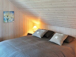 A bedroom with a bed, pillows, a nightstand, a lamp, and a wall painting. - Holiday Home in Gelting (Gelting)
