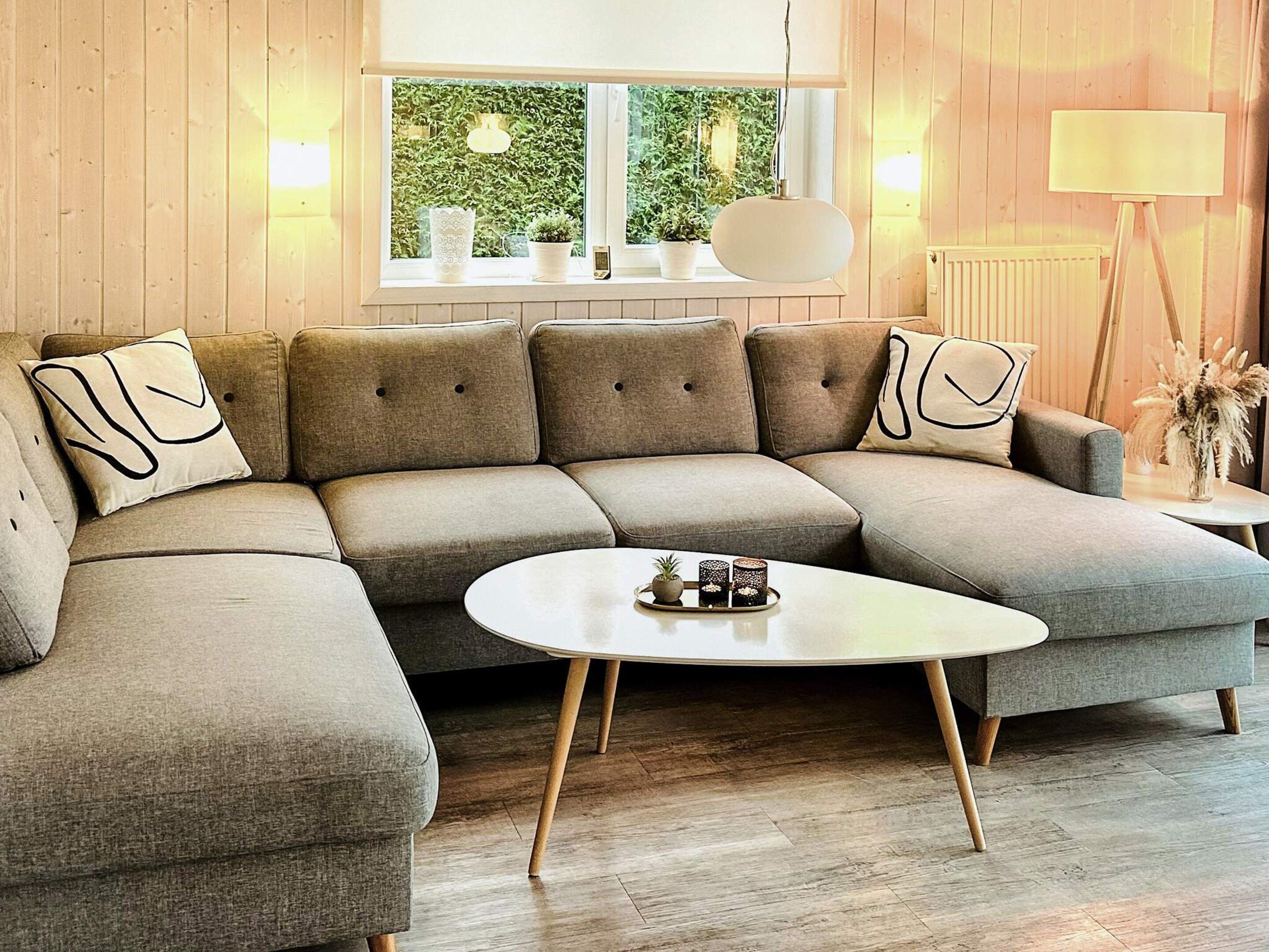 A modern living room with a sectional sofa, a round coffee table, and a view of greenery through a window.