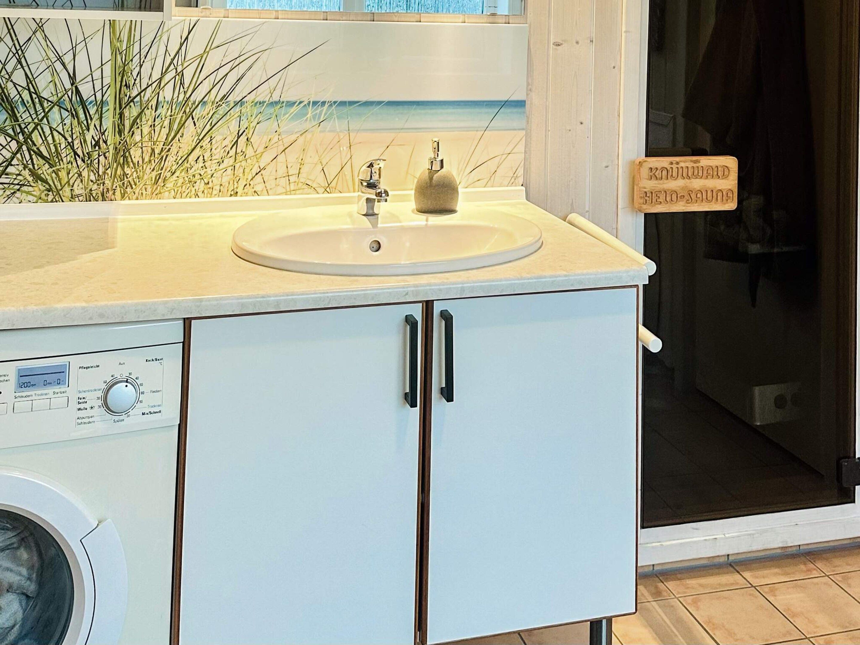 A bathroom with a sink, a washing machine, and a sauna sign.