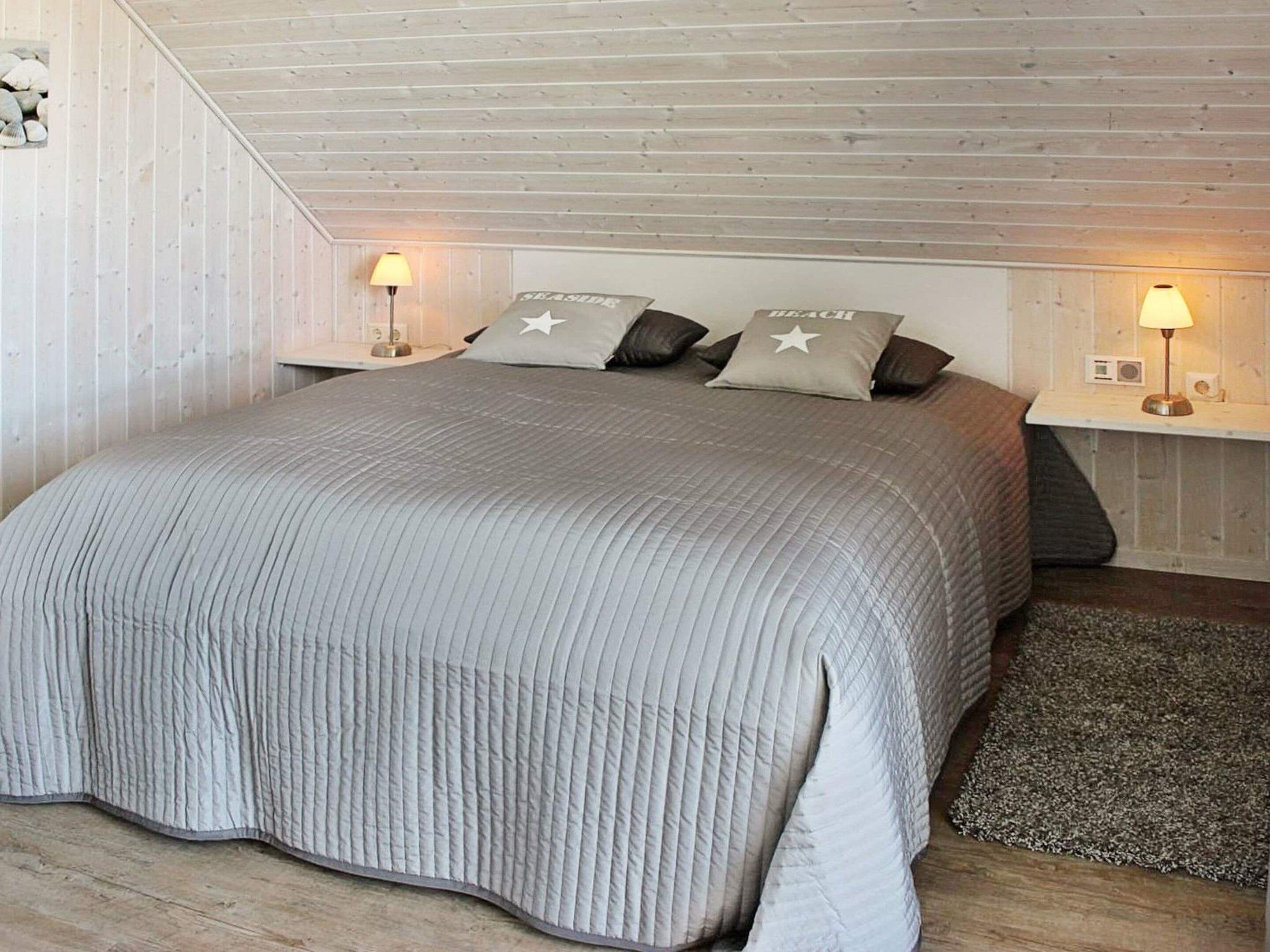 A bedroom with a large bed, two bedside tables with lamps, and a wooden ceiling.