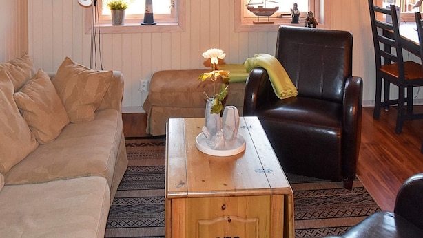 A cozy living room with a sofa, a wooden coffee table with a vase of flowers, a leather armchair, and a patterned rug. - 5 Person Holiday Home in Bud-by Traum (Hustadvika)