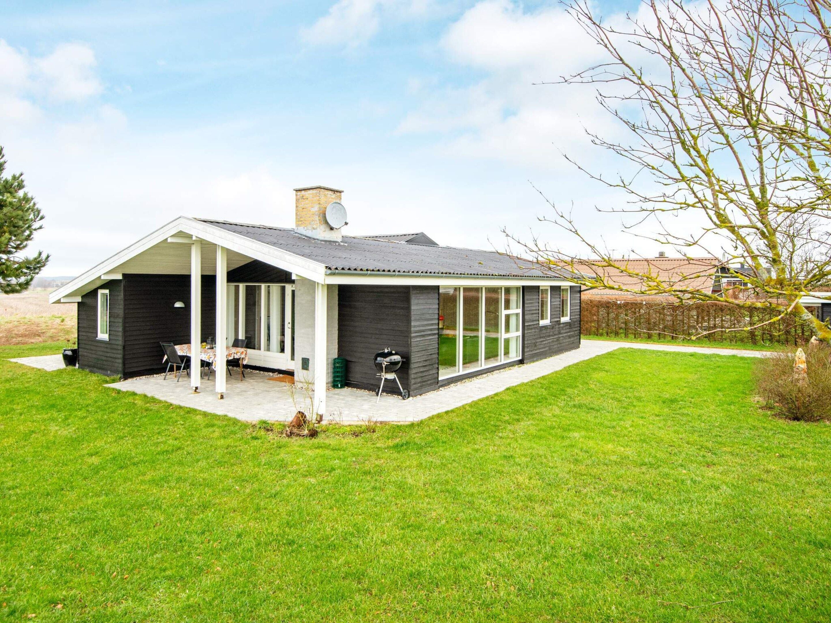 A modern house with a covered patio, a barbecue grill, and a well-maintained lawn.