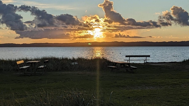 A sunset over a body of water with a bench and picnic tables in the foreground. - 8 Person Holiday Home in Ebeltoft-by Traum (Ebeltoft)