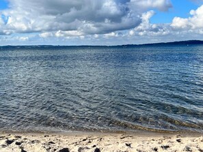 A beach with clear water, a sandy shore, and distant land.