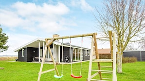 A wooden swing set with a ladder, a house with a covered porch, and a tree in a grassy yard. - 8 Person Holiday Home in Ebeltoft-by Traum (Ebeltoft)