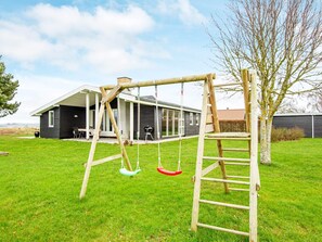 A wooden swing set with a ladder, a house with a covered porch, and a tree in a grassy yard. - 8 Person Holiday Home in Ebeltoft-by Traum (Ebeltoft)