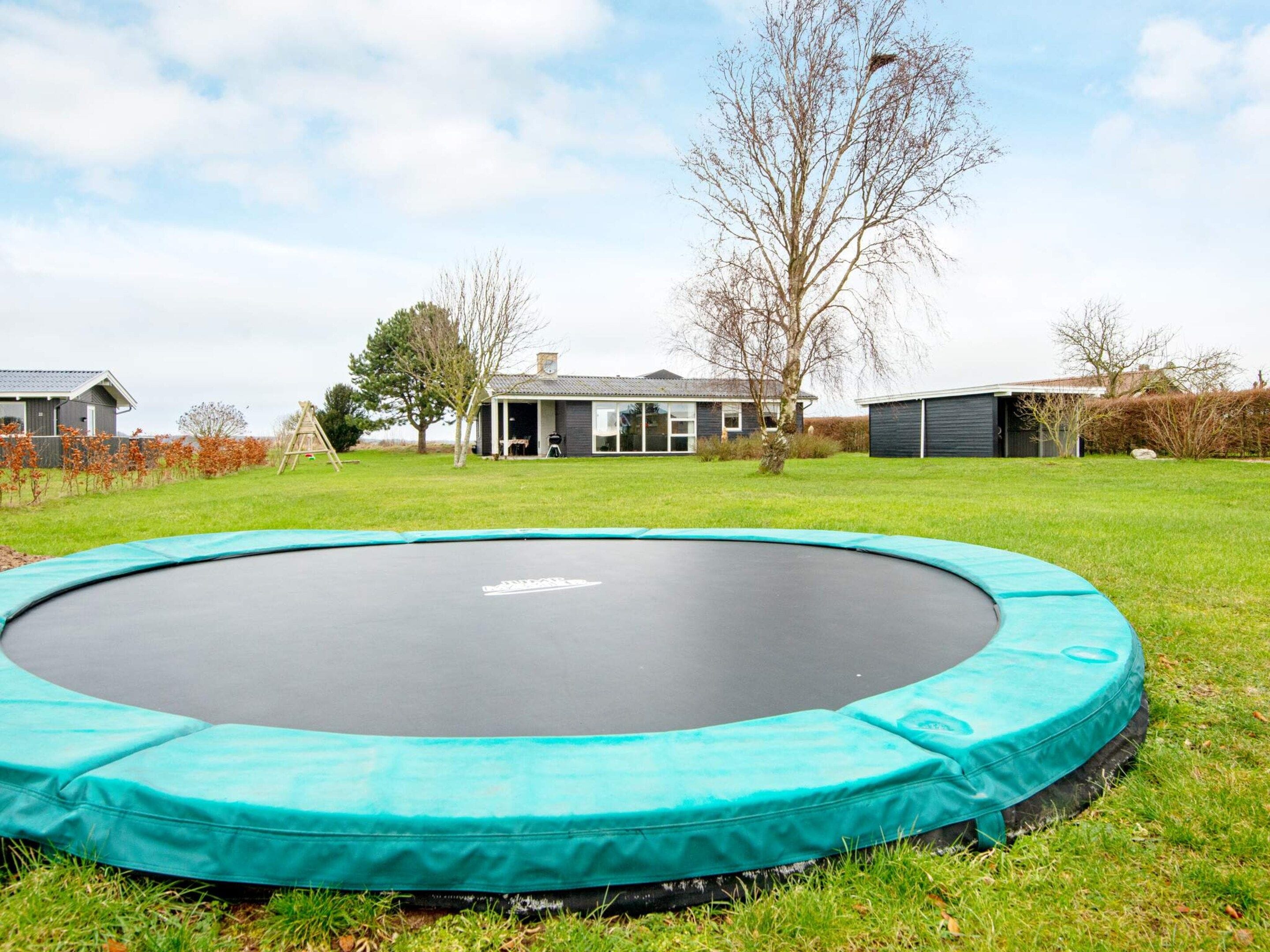 A trampoline in a grassy yard with a house in the background.
