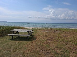 A picnic table by a beach with a view of the ocean and boats. - 8 Person Holiday Home in Ebeltoft-by Traum (Ebeltoft)
