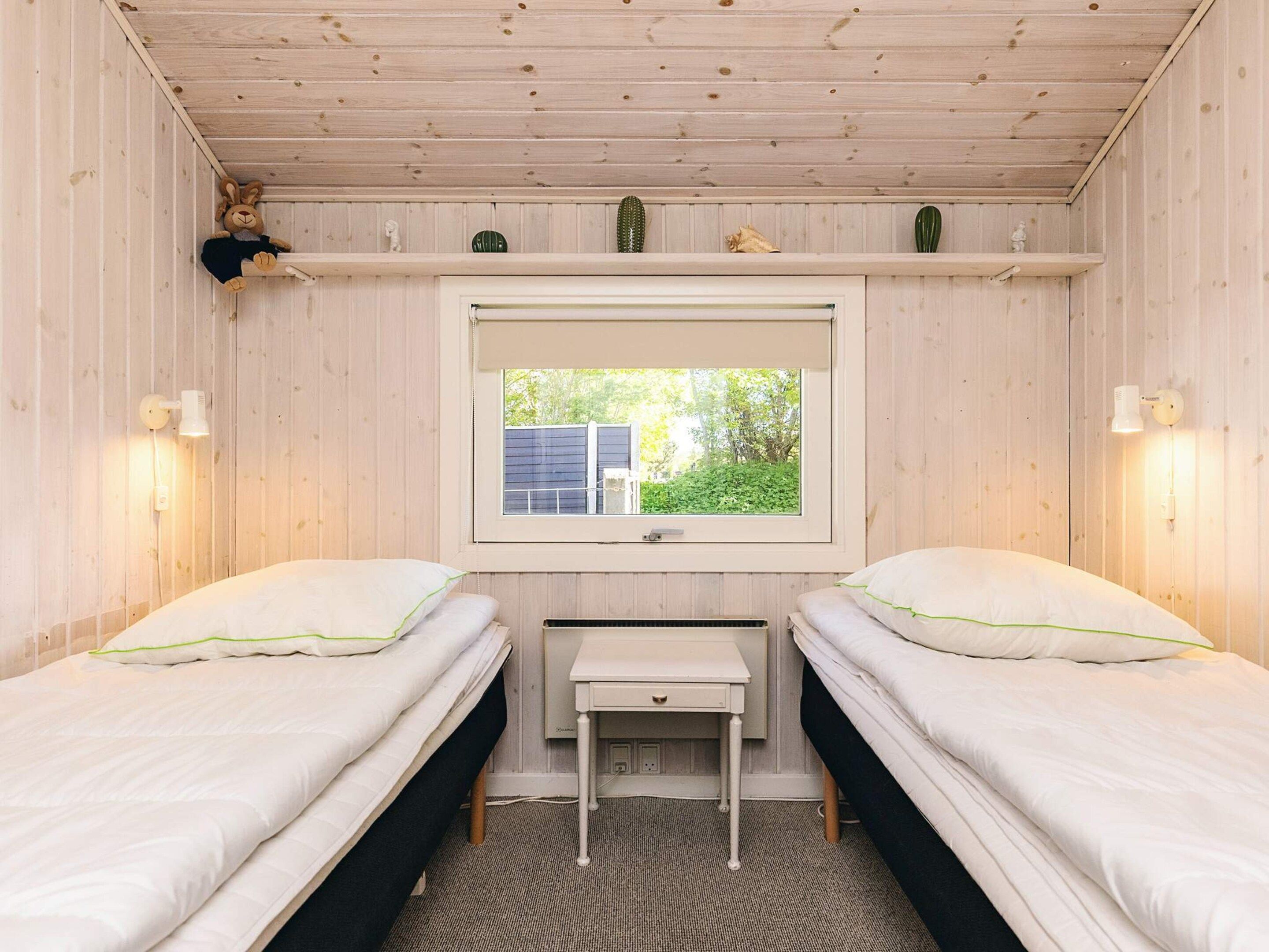 A room with two beds, a window, a desk, and a shelf with decorative items.