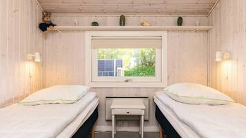 A room with two beds, a window, a desk, and a shelf with decorative items.