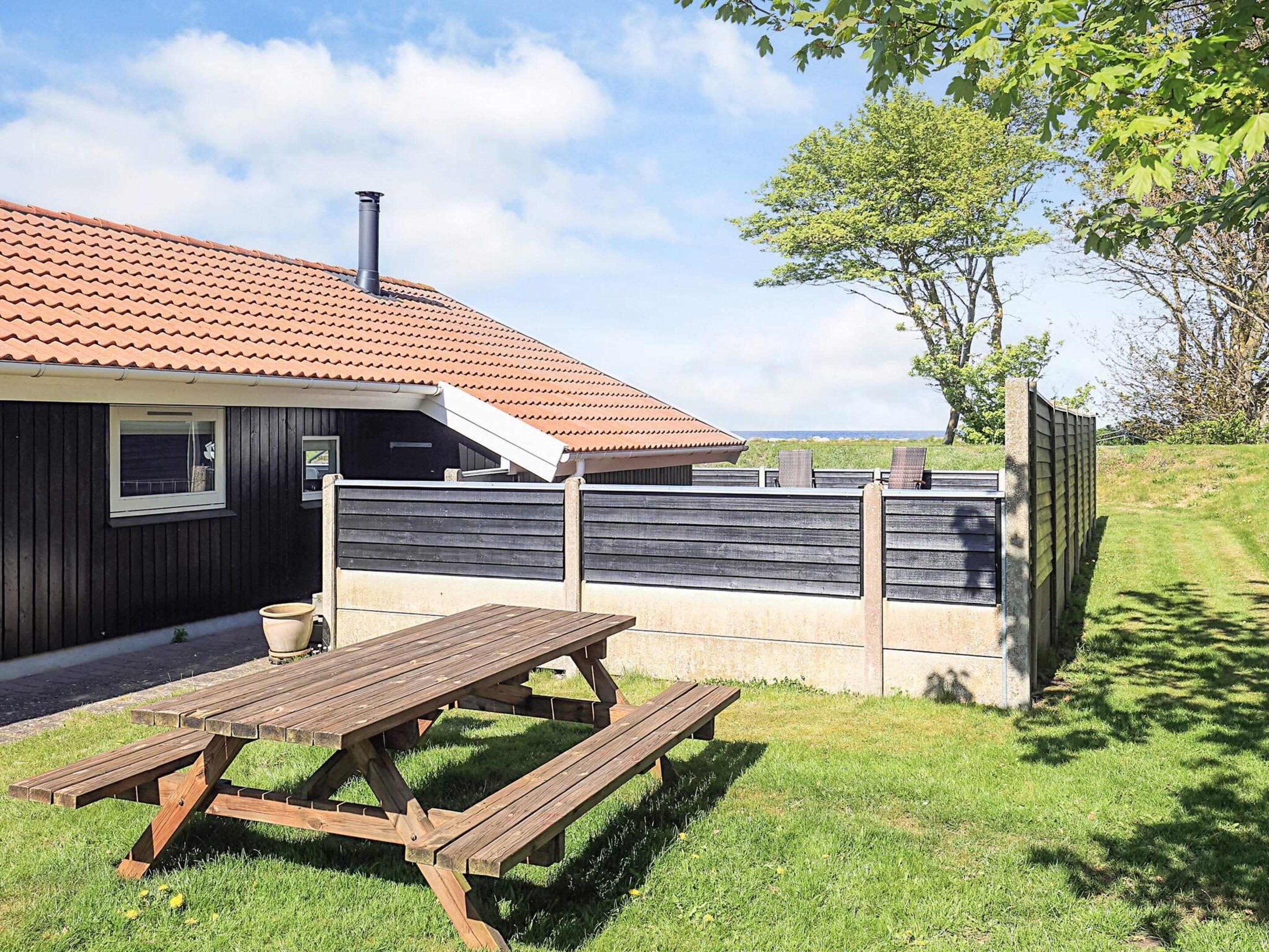 Ein Haus mit Ziegeldach, einer Holzterrasse und einem eingezäunten Garten.